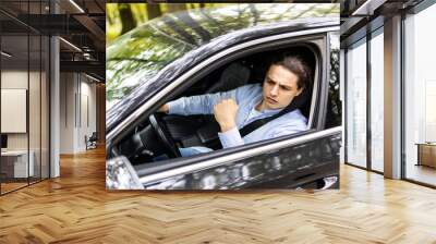 Annoyed tired young man is riding driving car. Businessman is late for meeting. Driver brunette in grey suit stuck in traffic jam. Stressful situations on roads and fast rhythm in modern city. Wall mural